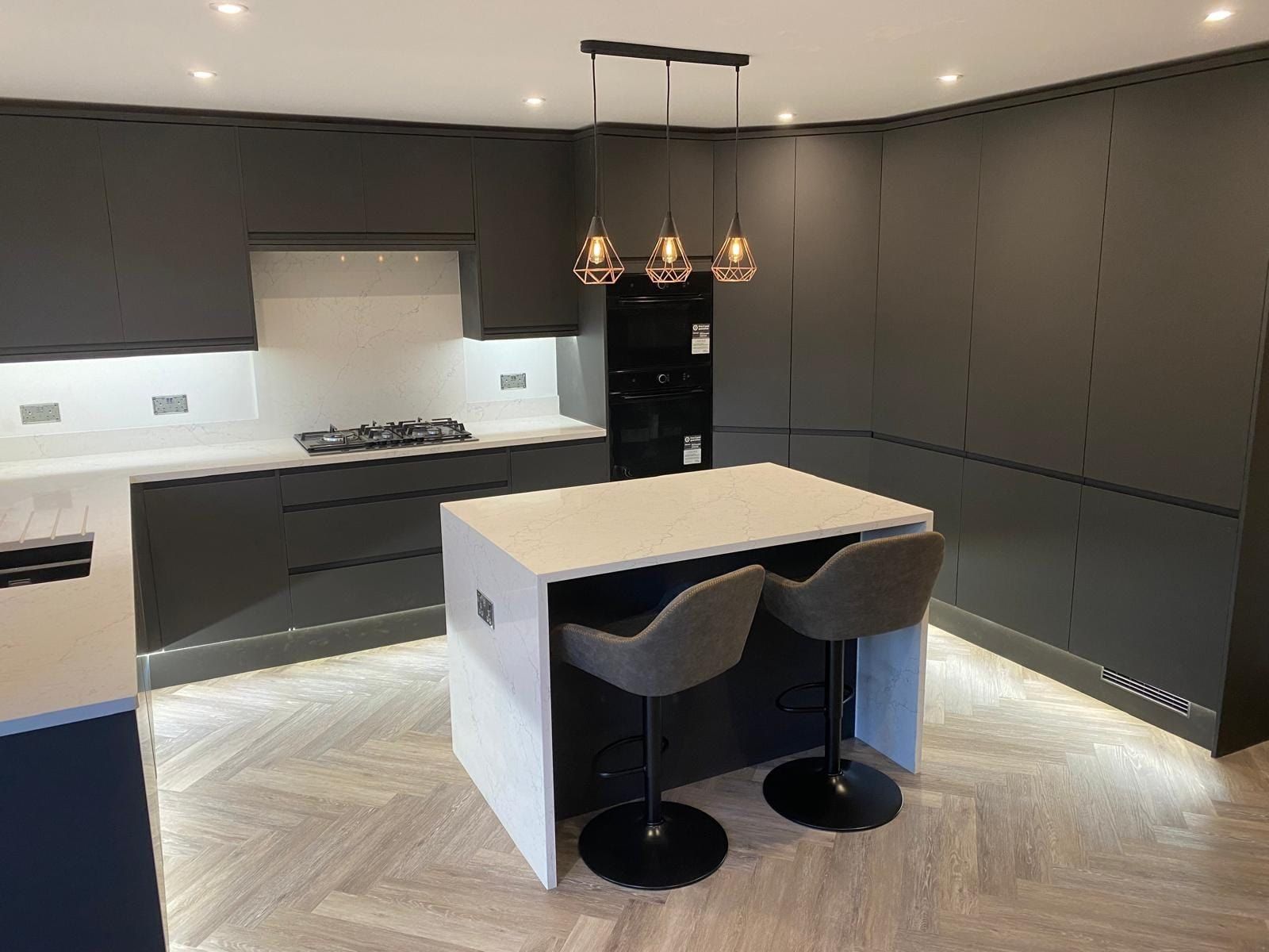 Dark handleless kitchen with a waterfall island and herringbone floor